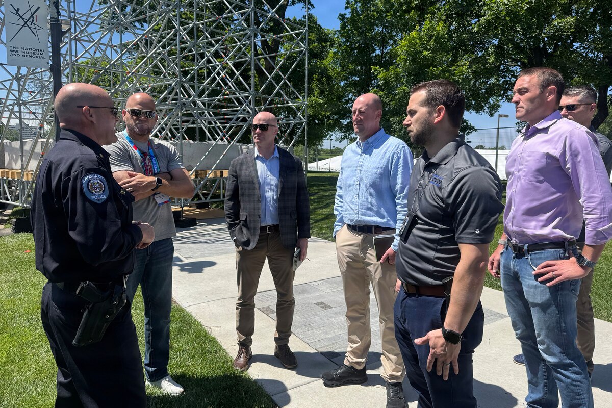 A police officer wearing a black uniform speaks to a group of men in casual attire outdoors.