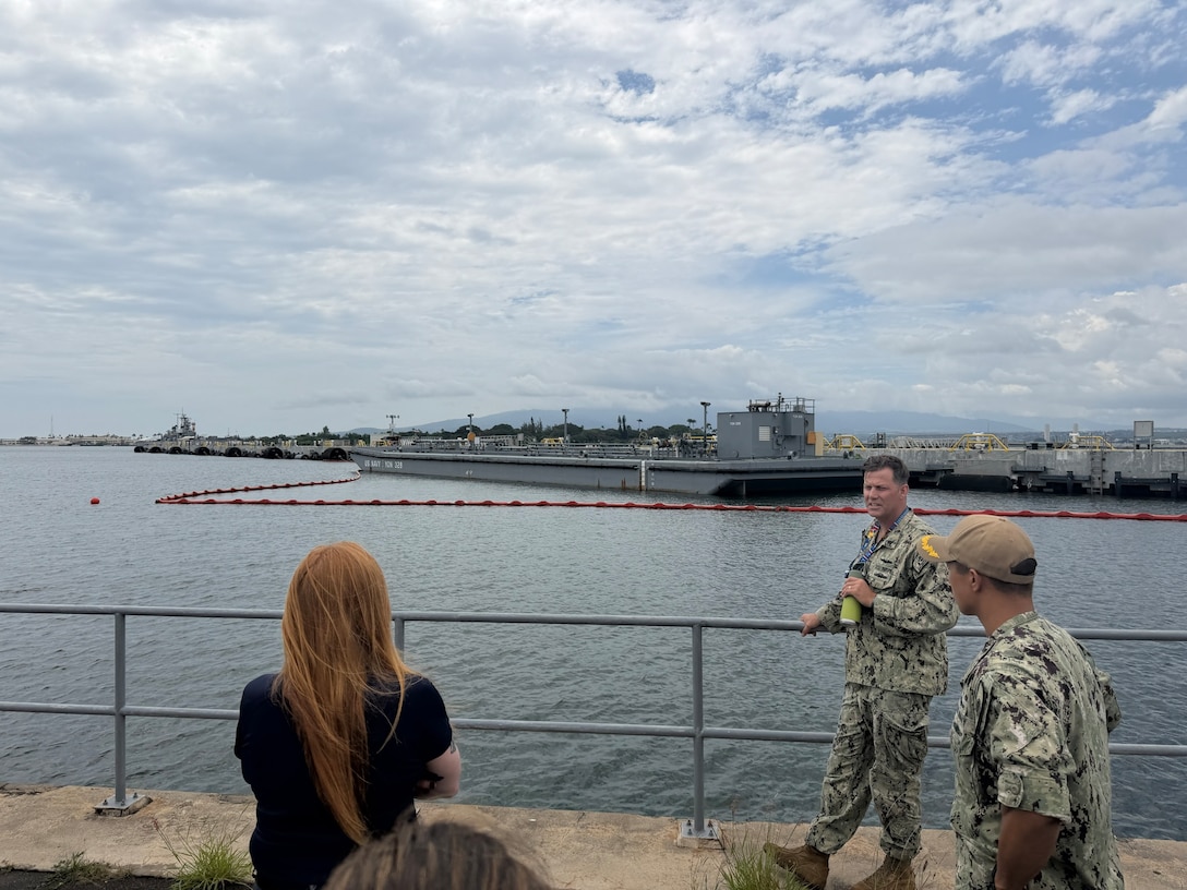 A Navy sailor stands against the railing at a port