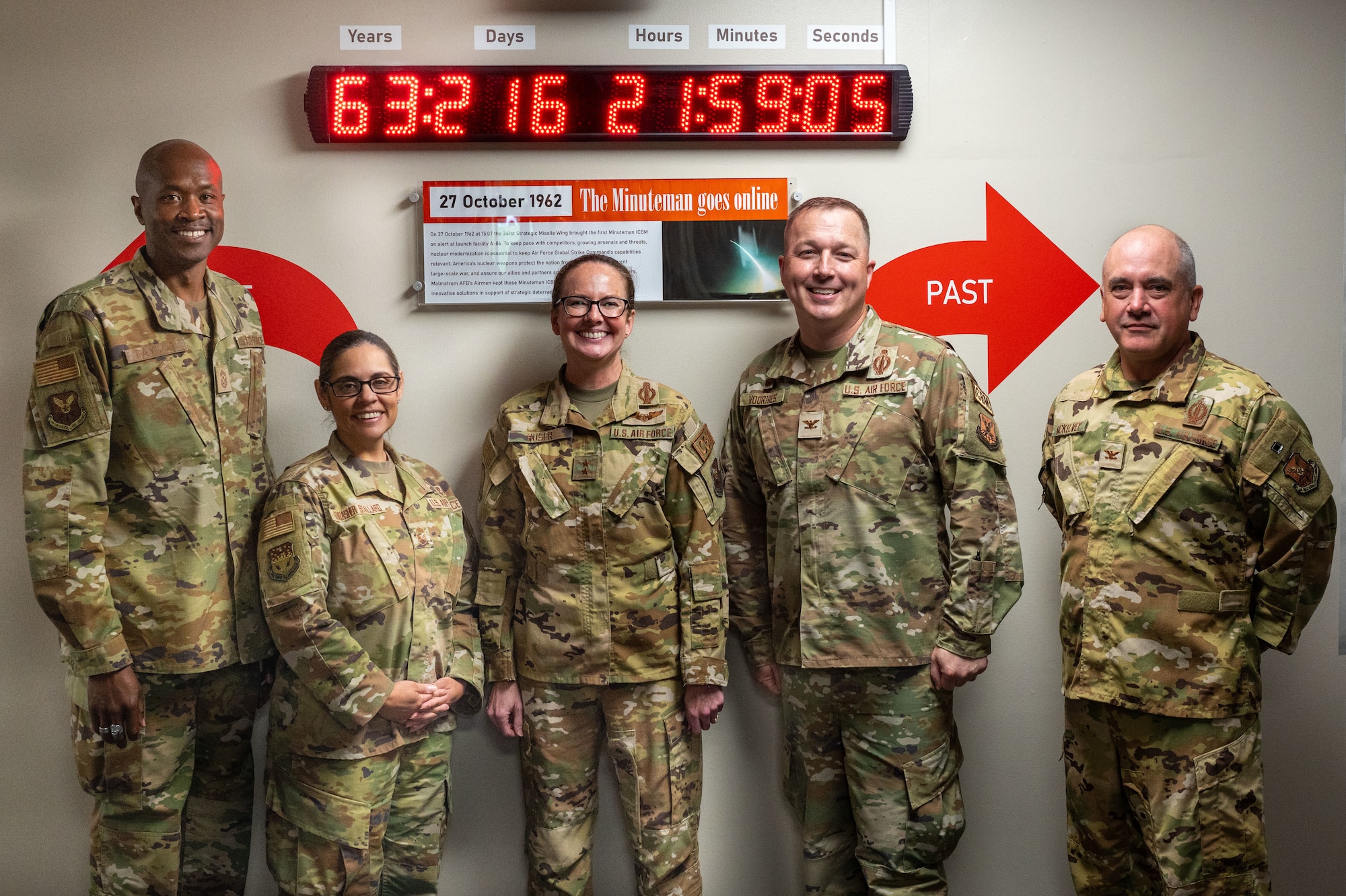 U.S. Air Force Maj. Gen. Stacy Jo Huser, center, 20th Air Force commander, and Chief Master Sgt. Nicholas Taylor, left, 20th Air Force command chief, pose for a photo with the 341st Missile Wing’s leadership team in front of the “First Ace in the Hole” clock at Malmstrom Air Force Base, Montana, June 1, 2026.