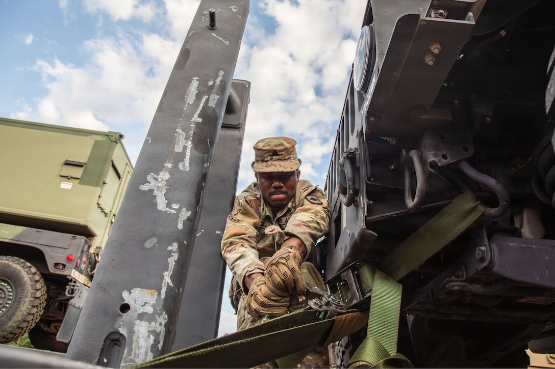 A soldier reaches to adjust a tie that is helping to secure a vehicle to a trailer.