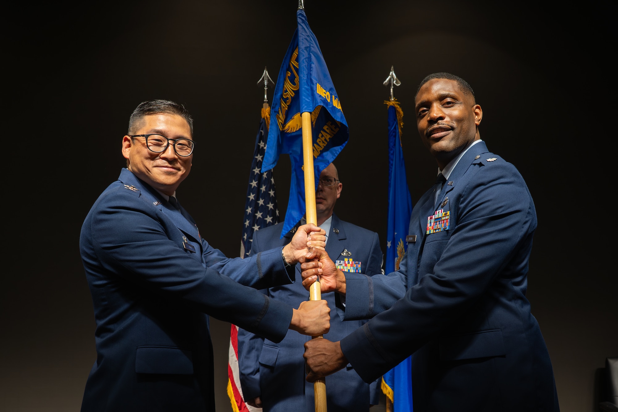 Col. Gene H. Noh, Forces and Technologies Intelligence Group commander, passes the Information Warfare Analysis Squadron (FTW) guidon to Lt. Col. Ty Axson, incoming FTW commander, during a change of command ceremony at the Air Force Institute of Technology, Wright-Patterson Air Force Base, Ohio, June 5, 2026. The passing of the guidon is a military tradition that symbolizes the official transfer of authority and command responsibility from the outgoing to the incoming leadership. (U.S. Air Force photo by Staff Sgt. Kristof J. Rixmann)