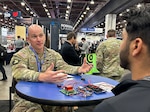 A U.S. Army Soldier sits at a table with electronic components and speaks to potential vendor.