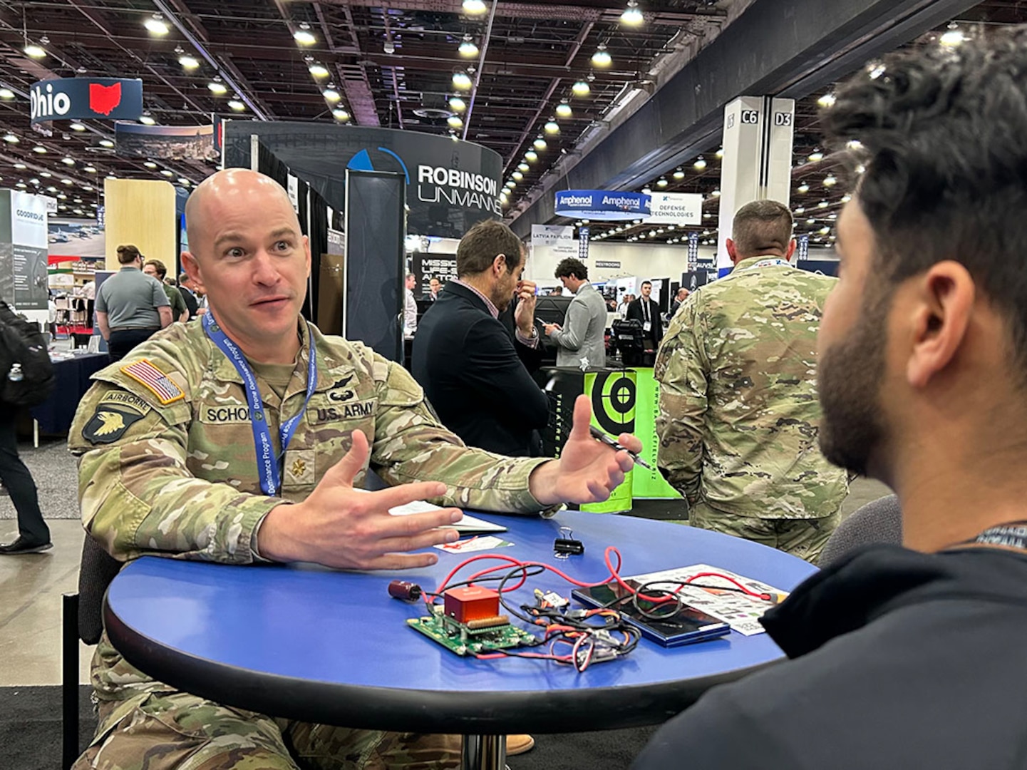 A U.S. Army Soldier sits at a table with electronic components and speaks to potential vendor.