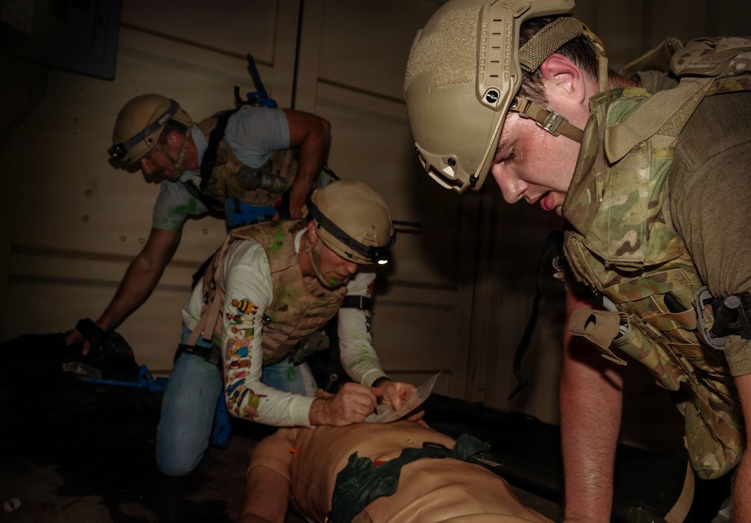 Airmen stand over a training manikin.