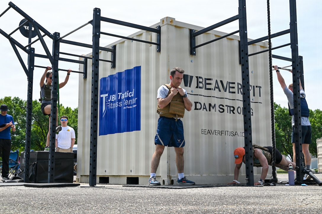 Group of workout participants surround a tan metal container and does different exercises.