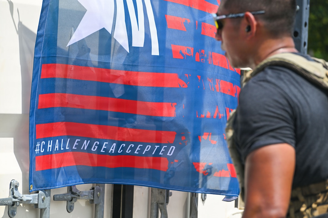 A flag with the words #challenge accepted hangs from a metal container.