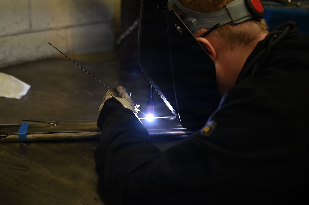 A man wearing protective face gear welds a large sword.