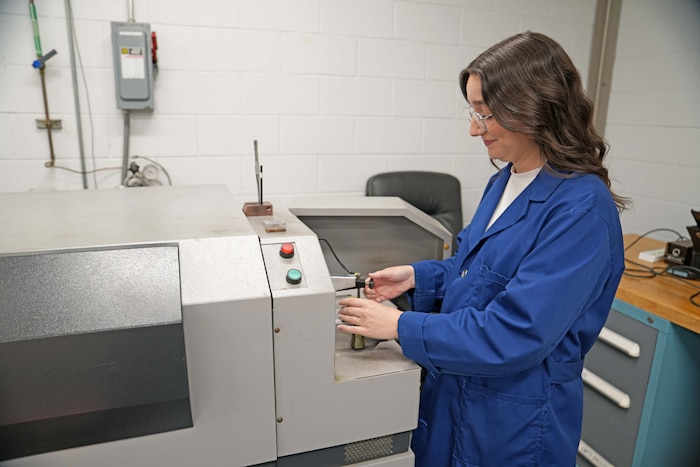 Photo shows woman using large machine to test a small part