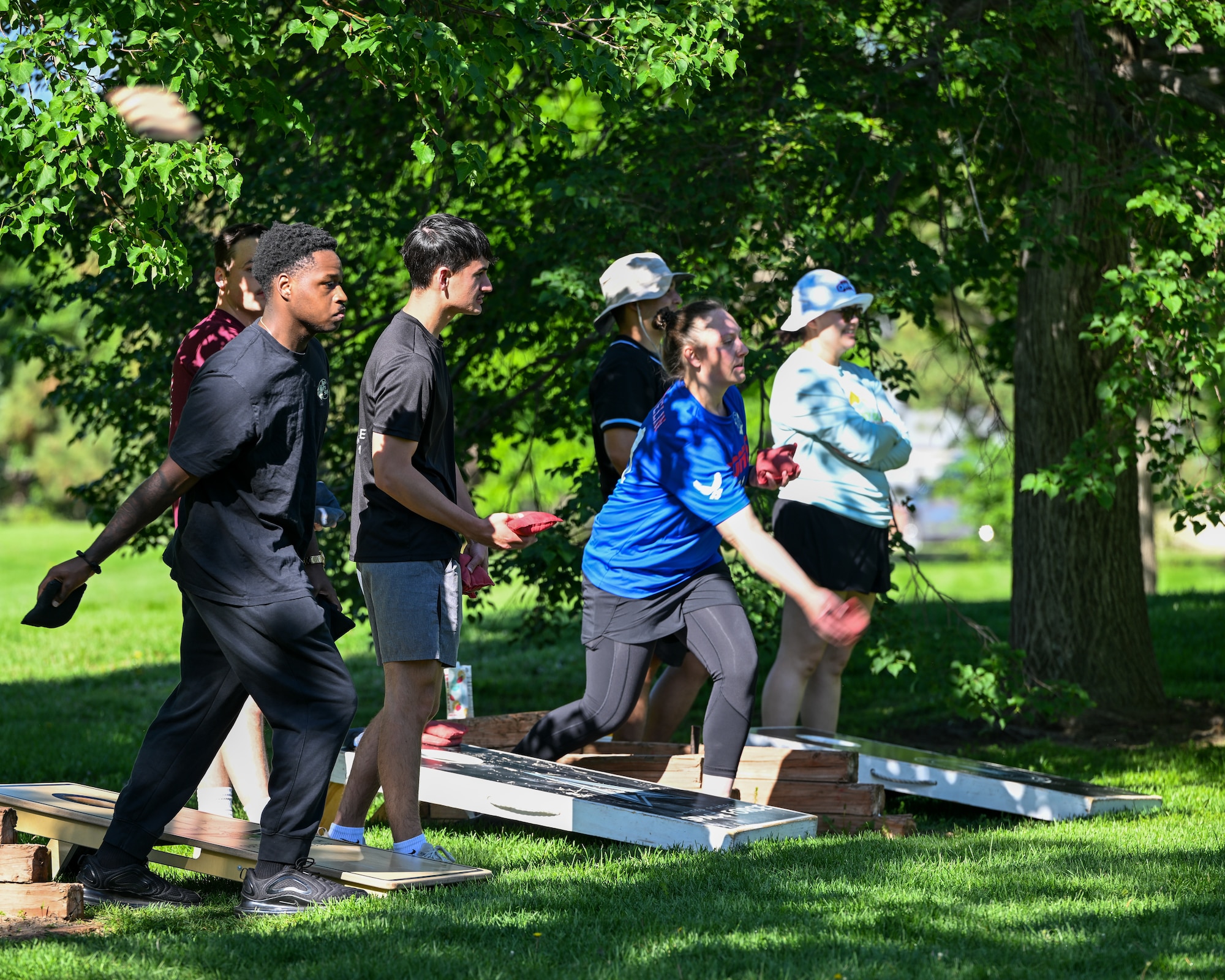 Players stand next to thier corn hole board throwing bean bags.