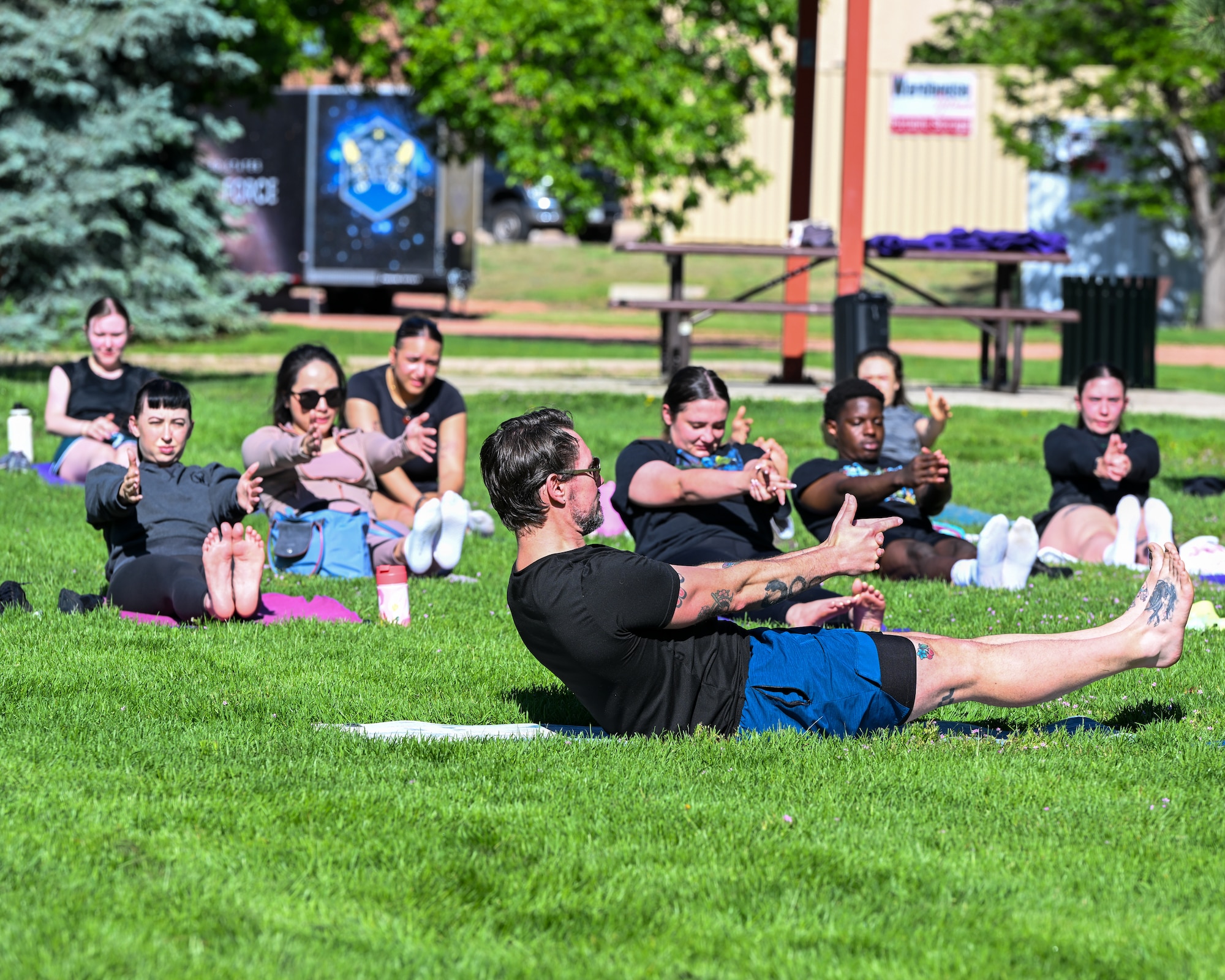 An instructor sits in front of participants leading a yoga class.