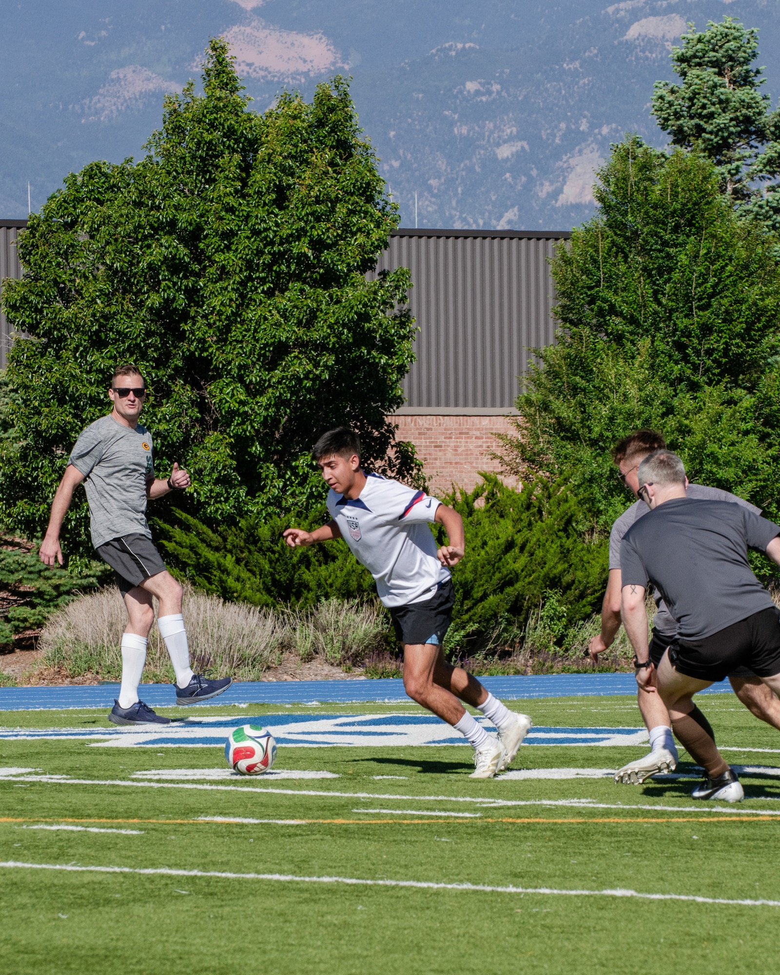 A player runs behind a soccer ball as others try to intercept or defend him.