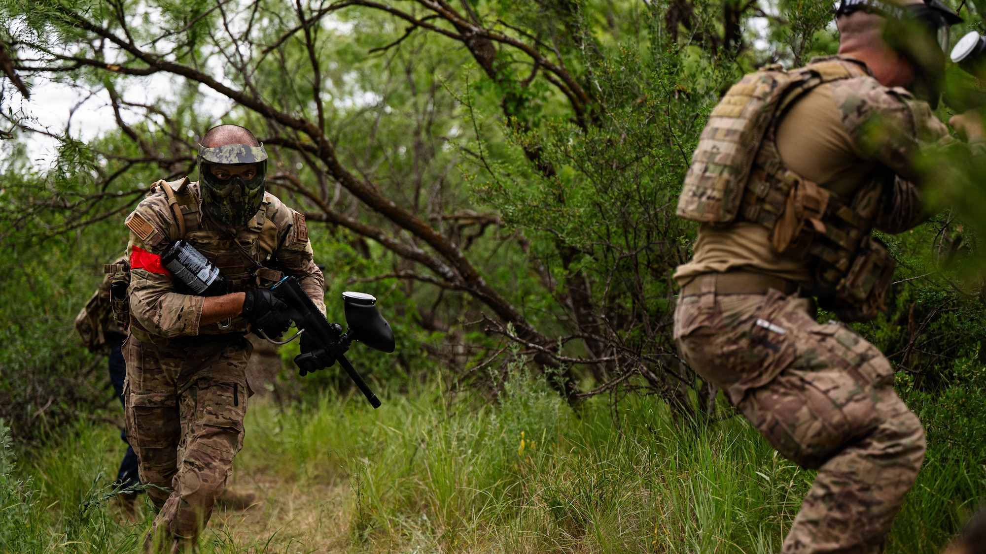 Airmen participate in a field exercise and play capture the flag outside in a wooded area