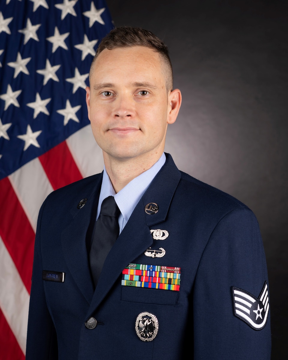 Official Photo of Staff Sergeant Erik Lofgren, Piano, United States Air Force Bands. SSgt Lofgren is wearing navy blue service dress in front of an American flag.