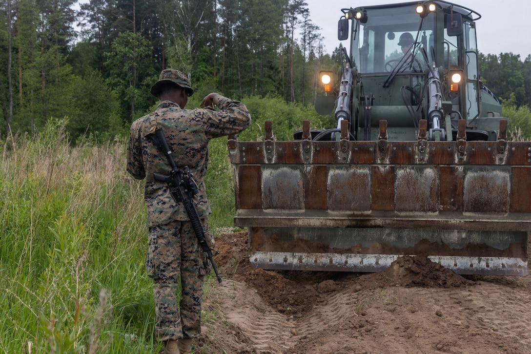 U.S. Marine Corps Cpl. Joseph Fraser, left, an engineer equipment mechanic, ground guides Cpl. Garrett Heffner, an engineer equipment operator, both with Combat Logistics Battalion 24, Combat Logistics Regiment 27, 2nd Marine Logistics Group, during road repair operations as part of exercise Baltic Operations 26 in Skrunda, Latvia, June 5, 2026. BALTOPS 2026, the premiere maritime-focused exercise in the Baltic Region, provides a unique training opportunity to strengthen combined response capabilities critical to preserving freedom of navigation and security in the Baltic Sea. Heffner is a native of Illinois. Fraser is a native of Florida. (U.S. Marine Corps photo by Lance Cpl. Talan Werner)
