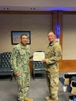 Travis Air Force Base – Chief Petty Officer Darren Hallhuz (left), a missile technician assigned to Defense Threat Reduction Agency (DTRA) Global Threat Reduction Directorate (GT), receives the Navy and Marine Corps Achievement Medal on May 20, 2026 at Travis Air Force Base in Fairfield, California.  The award was presented by Lt. Col. Ronald J. Barnhart (right), DTRA GT’s Travis commanding officer,  on behalf of Portfolio Acquisition Executive Strategic Systems Programs Program Management Office (PMO) Flight Systems detachment (SPF(S)) in recognition of Hallhuz’s exceptional support to the U.S. Navy submarine force throughout SPF(S)’ Reverse Strategic Weapons Systems (SWS) Week. (U.S. Navy photo by Shelby Thompson//Released)