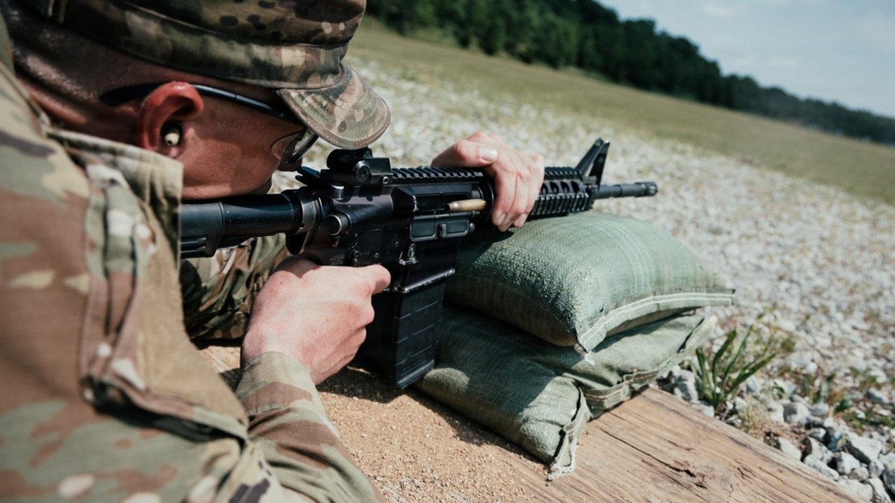 A soldier lies on the ground and aims a weapon.