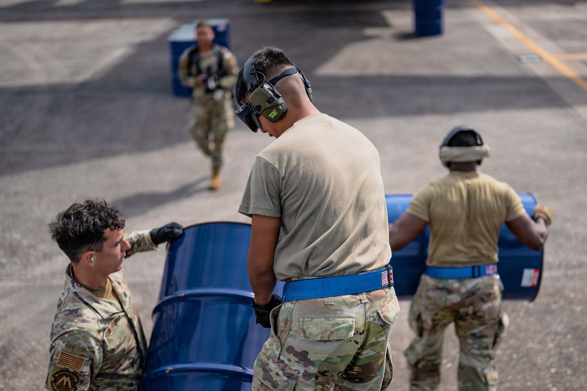 Three military members carry blue, 55-gallon drums
