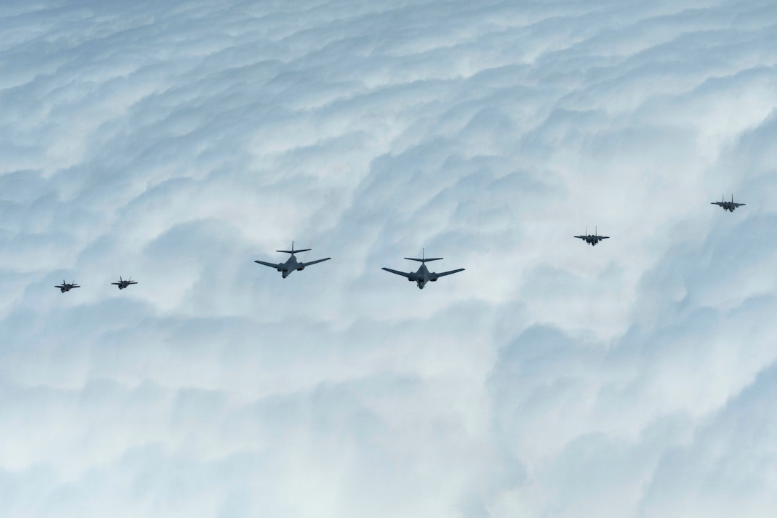 Six aircraft fly in formation over the clouds.