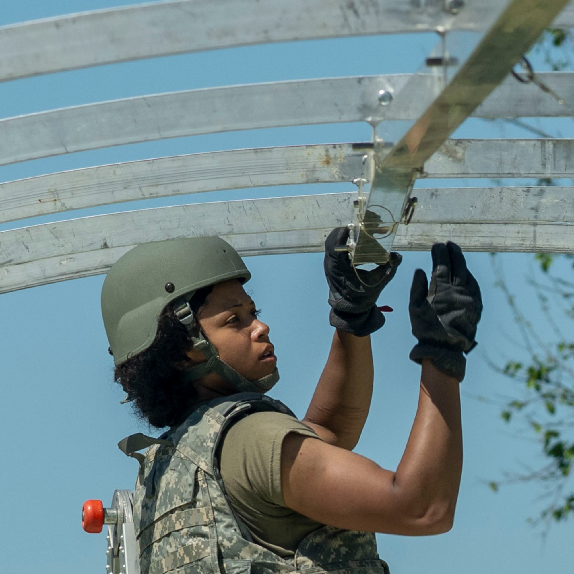An Airman wearing tactical gear reaches up to assemble metal tent pieces.