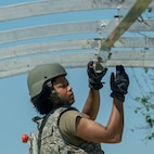 An Airman wearing tactical gear reaches up to assemble metal tent pieces.