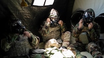 Three Airmen sit in a tent tightening gas masks.