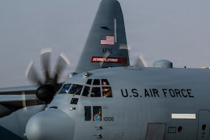 A military aircraft taxis on a flight line. The pilots are in the cockpit.