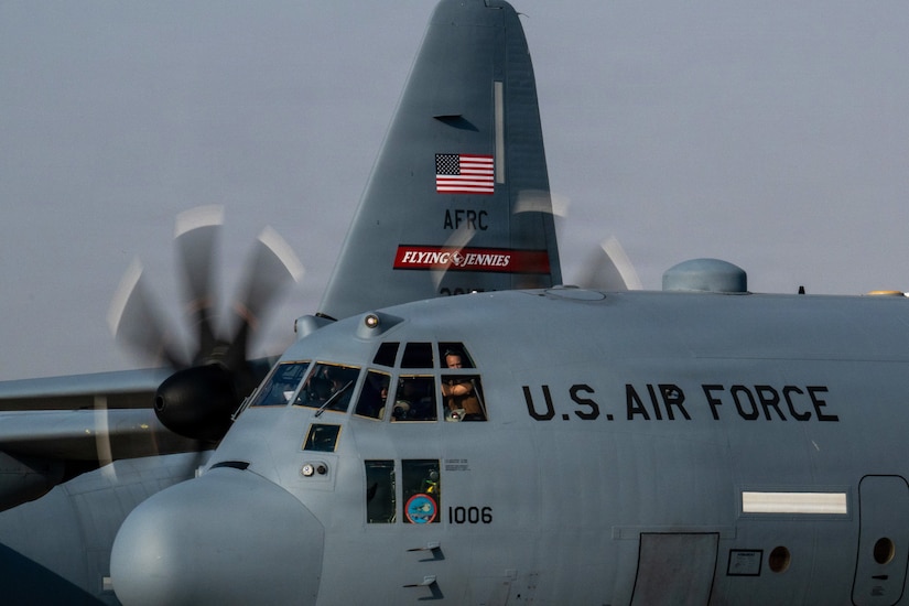 A military aircraft taxis on a flight line. The pilots are in the cockpit.