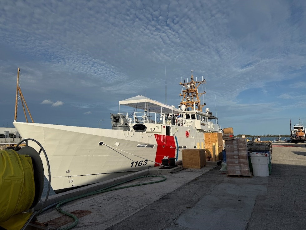 A fast response cutter is at a dock with wooden boxes and other marine equipment in front of it.