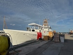 A fast response cutter is at a dock with wooden boxes and other marine equipment in front of it.
