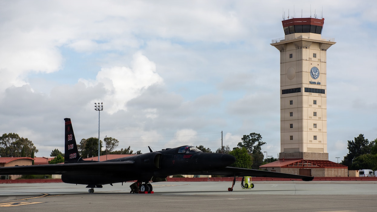 Aircraft is parked on flight line with air traffic control tower in the background