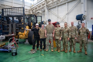 A group of people stand in front of a forklift.