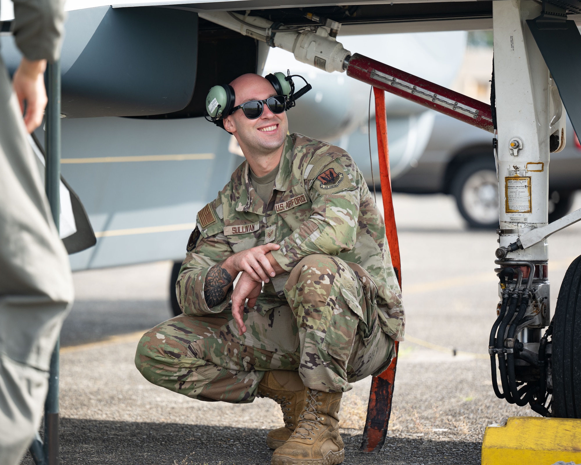 A servicemember crouches under the wing of an aircraft