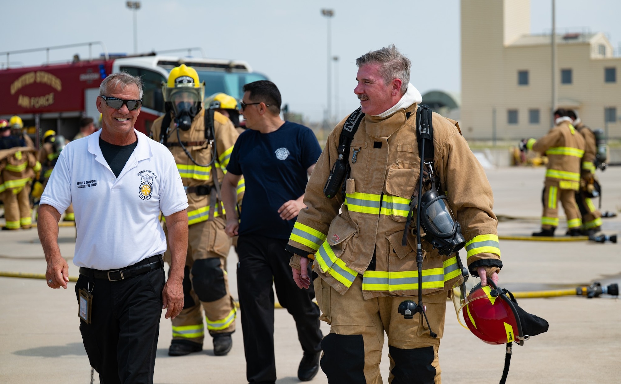 A man walks with another person in firefighter gear with fireman in the background.