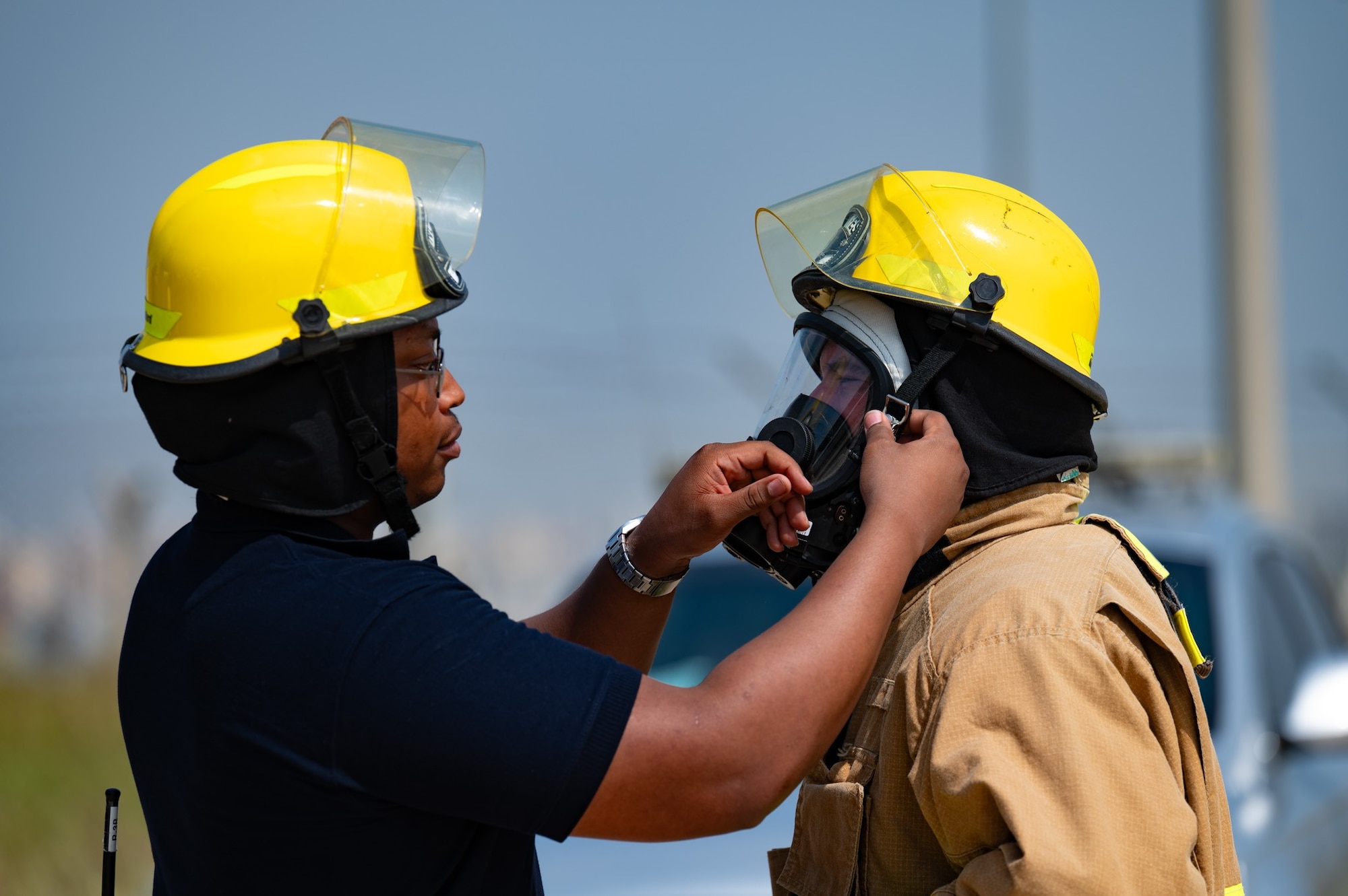 A firefighter helps someone put on a firefighter helmet.