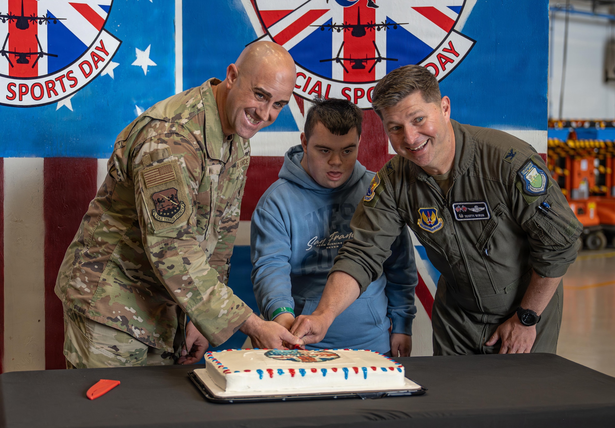 U.S. Air Force Chief Master Sgt. James Wall, left, 100th Air Refueling Wing command chief and Col. Steven Byrum, right, 100th ARW commander, cut the cake with one of the competitors during Joan Mann Special Sports Day at RAF Mildenhall, England, June 4, 2026.
