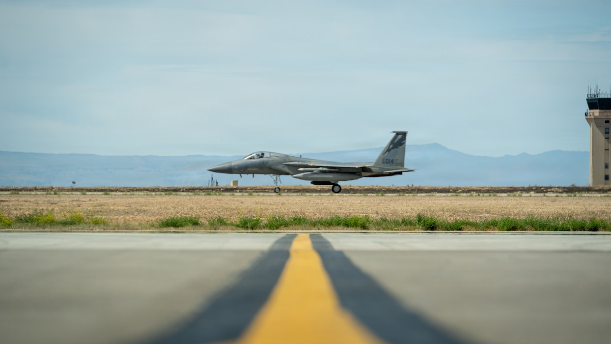 An F-15C Eagle parked on base with mountain view in the back and yellow strip toward to the plane.