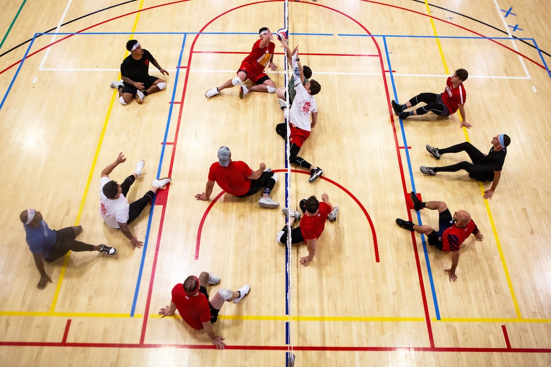 Marines and veterans play a seated game of volleyball in an indoor basketball court as seen from above.