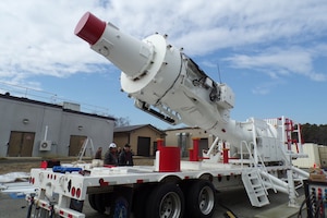 A large, white antenna sits on a flatbed truck outside under a blue sky before it is installed.
