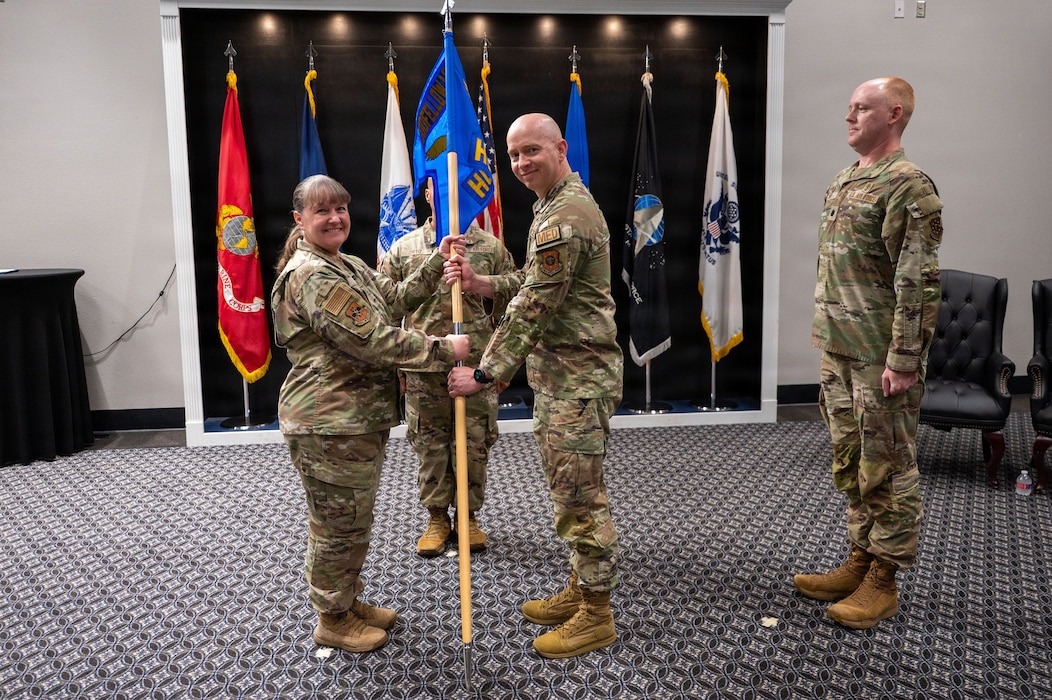 Two military members smile while exchanging a guidon.