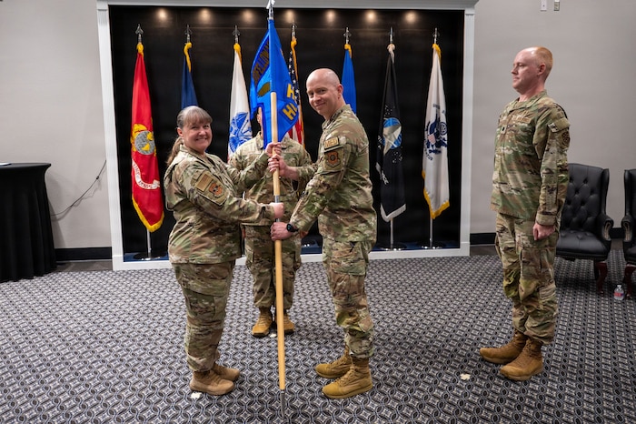 Two military members smile while exchanging a guidon.