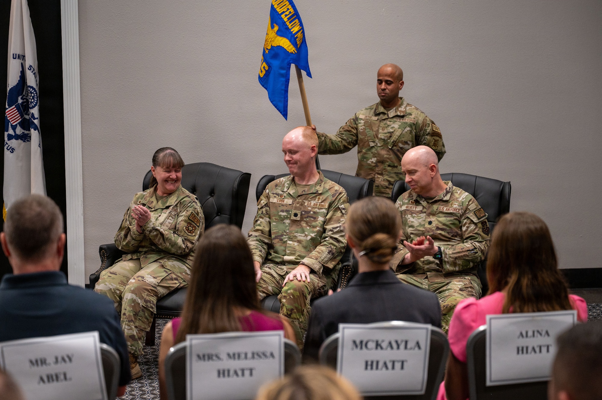 A row of three uniformed members are sitting and clapping.