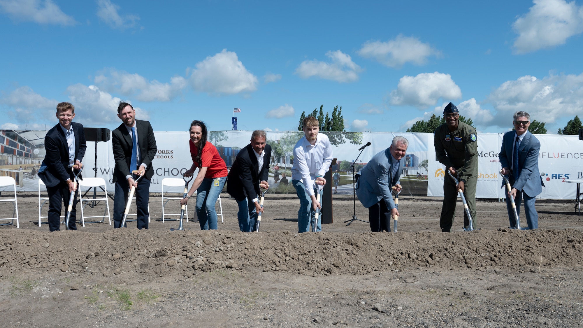 Eight people shovel dirt on a construction site.