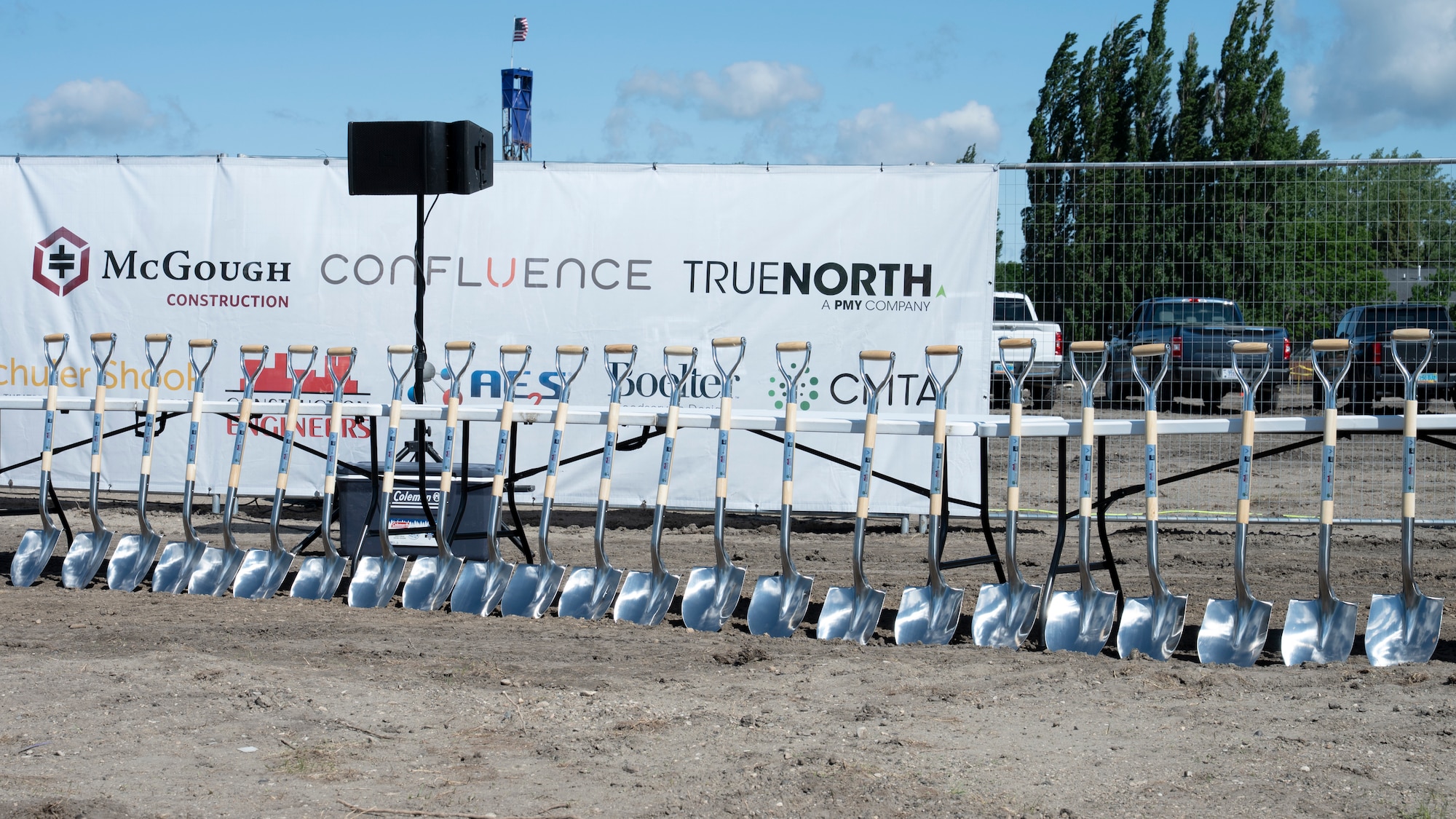 Twenty-three shovels are lined up on a construction site.