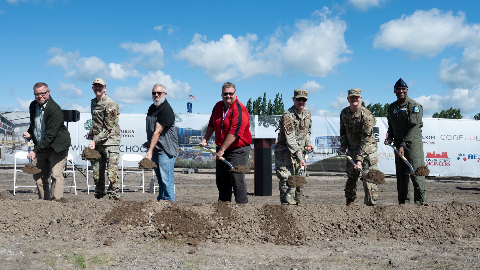 Seven men hold silver shovels and scoop brown dirt