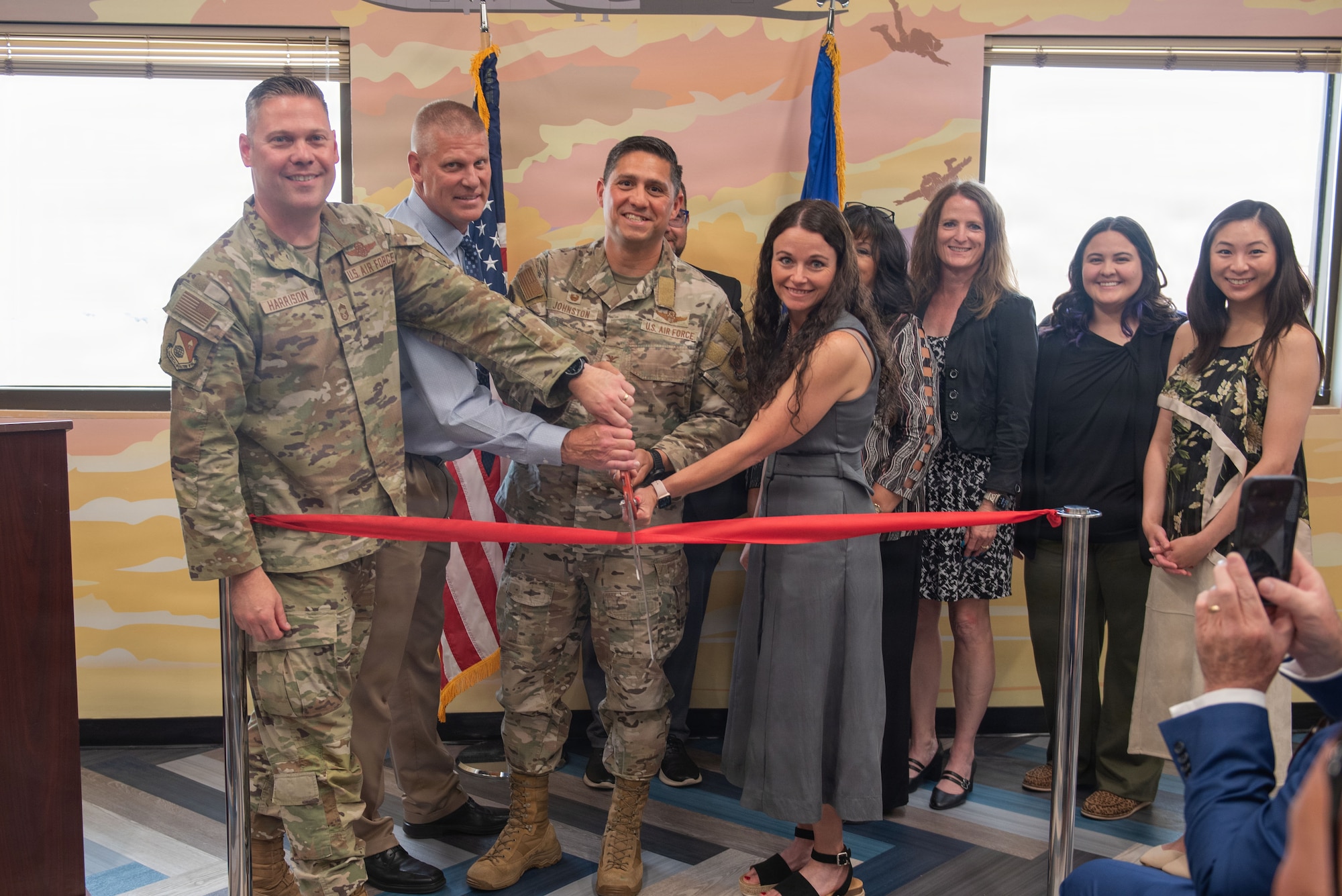 People stand behind a ribbon with a large pair of scissors.