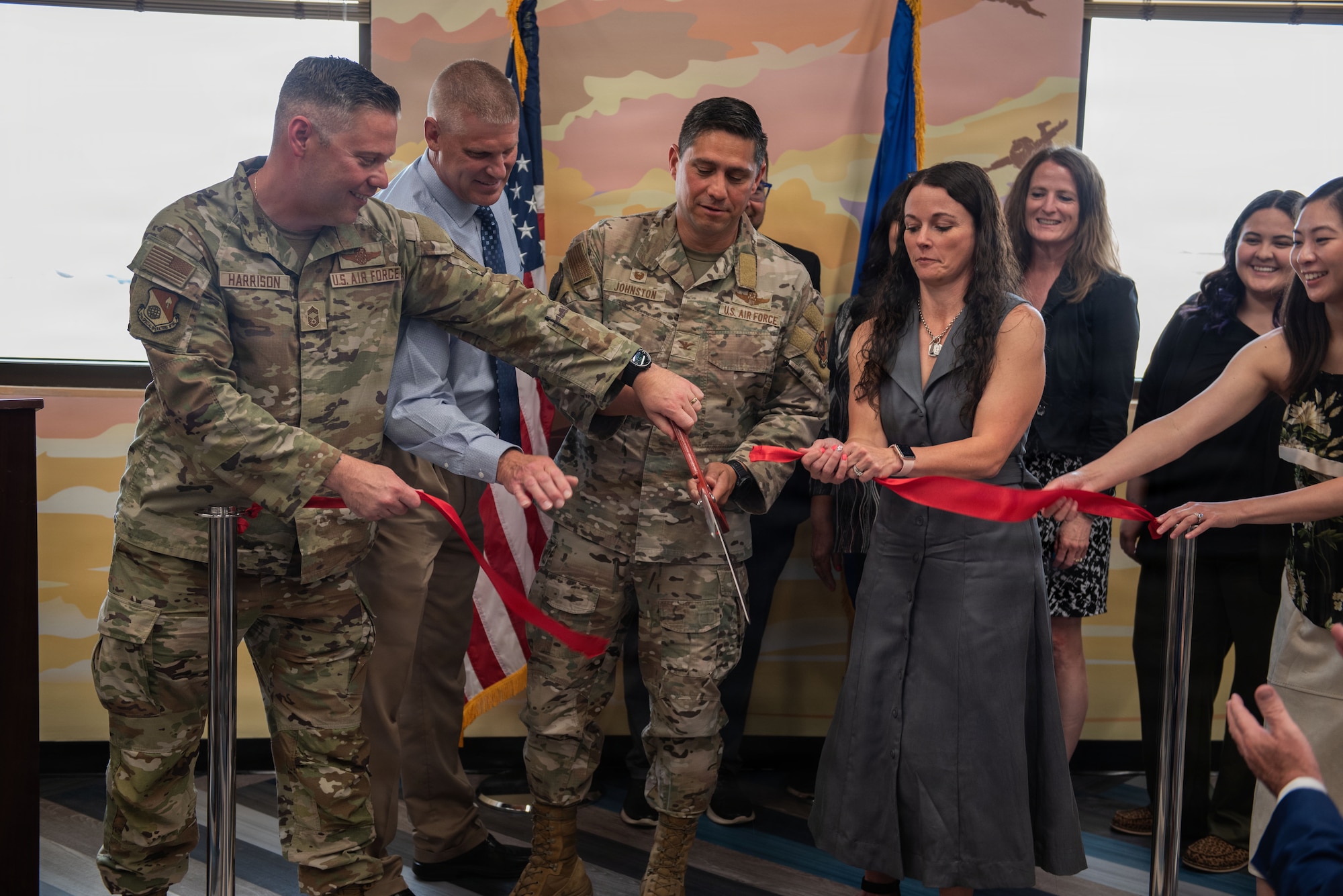 A group of people cut a red ribbon in front of a painted wall.