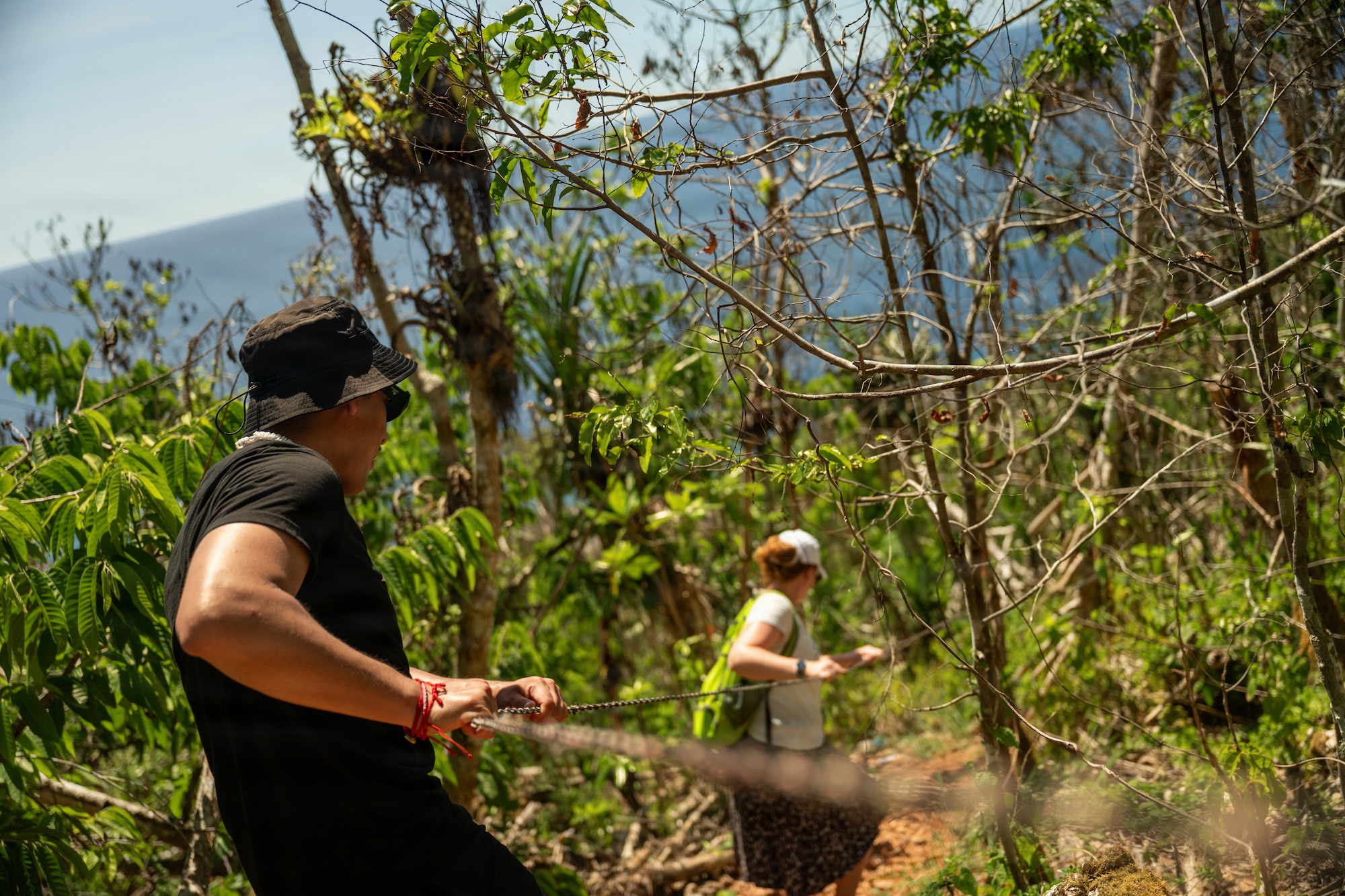 U.S. Air Force Senior Airman Luis Huallpa Jurado, 439th Communications Squadron radio frequency technician and Staff Sgt. Ashley Bowman, 439th Aeromedical Evacuation Squadron expeditionary communications technician, holds onto a guide line while navigating steep terrain during Cyber Guam 2026 near Dededo, Guam, June 8th, 2026.