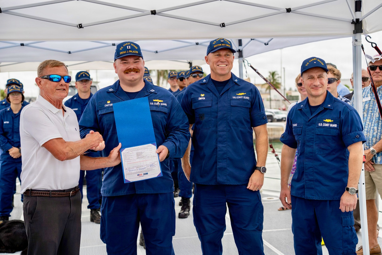Lt. Hayden Carter (second from left), commanding officer of USCGC Jeffrey Palazzo (WPC 1163), shakes hands with Allen Harker (left), contracting officer for the Fast Response Cutter Project, during an acceptance ceremony in Key West, Florida, on June 11, 2026. The cutter is named for Jeffrey Palazzo, a New York City firefighter and U.S. Coast Guard reservist who made the ultimate sacrifice on Sept. 11, 2001, while responding to the attacks on the World Trade Center. (U.S. Coast Guard photo by Ensign Carly Logan)