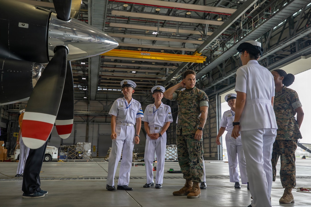 U.S. Marine Corps Lance Cpl. Elijah Gaskin, center, a marine aviation operations specialist assigned to Marine Transport Squadron, Headquarters and Headquarters Squadron (H&HS), Marine Corps Air Station Iwakuni, explains the features and capabilities of a UC-12W Huron aircraft, assigned to H&HS,  MCAS Iwakuni, to Japan Maritime Self-Defense Force cadets during an installation tour at MCAS Iwakuni, Japan, June 9, 2026. The tour gave JMSDF cadets an opportunity to engage with U.S. Marines and Sailors at MCAS Iwakuni and better understand the installation’s capabilities. (U.S. Marine Corps photo by Lance Cpl. Tyler Bassett)