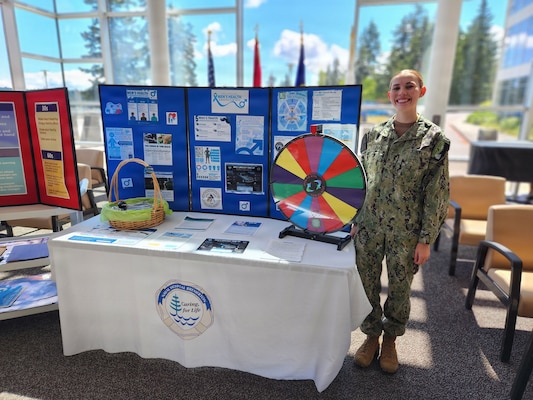 Hospitalman Karsyn Dalpiaz, assigned to Naval Hospital Bremerton, stands next to a display for a men’s health outreach event hosted by the Health Promotion and Wellness Center, June 10, 2026. Coordinated by the Health Promotion and Wellness team, educational resources and screening guidelines specifically focused on men’s cardiovascular health, mental wellness, and prostate cancer prevention were provided to support the long-term readiness and deplorability of Sailors, Marines, and civilian personnel. (U.S. Navy photo by Mass Communication Specialist 1st Class Jennifer Benedict, NHB/NMRTC Bremerton Public Affairs).